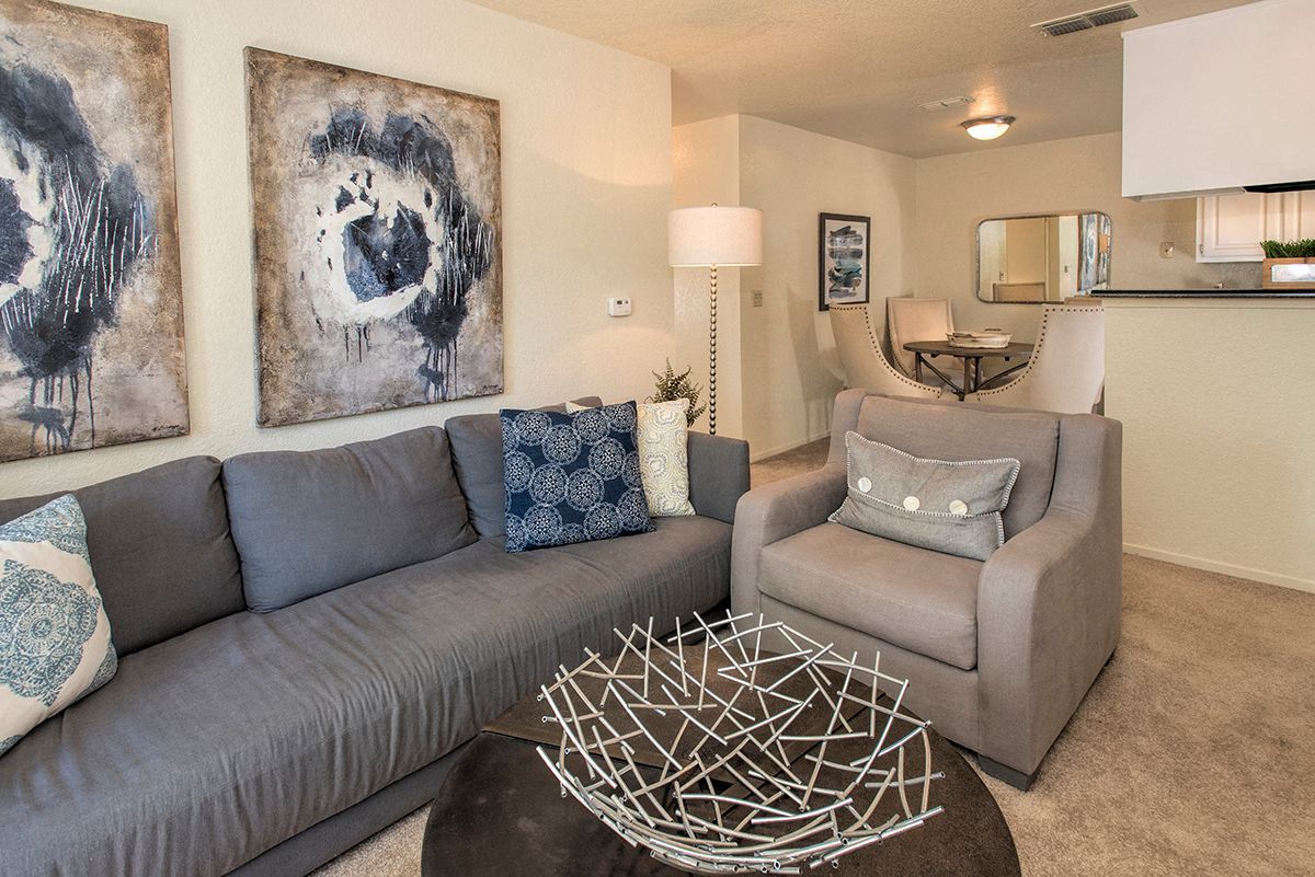 Living room in a modern apartment with a gray sofa, matching armchair, wall art, and a sculptural coffee table.