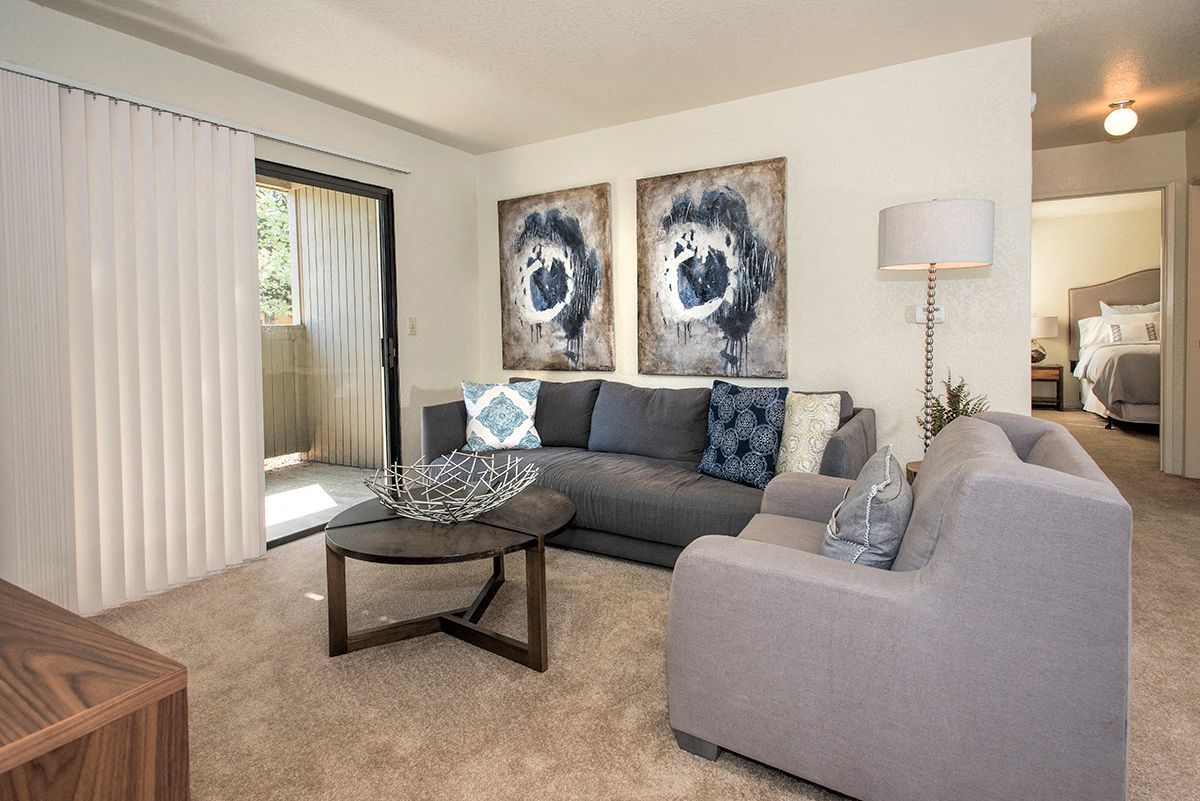 Living room with a gray sofa and chairs, round coffee table, and a sliding door to the balcony.