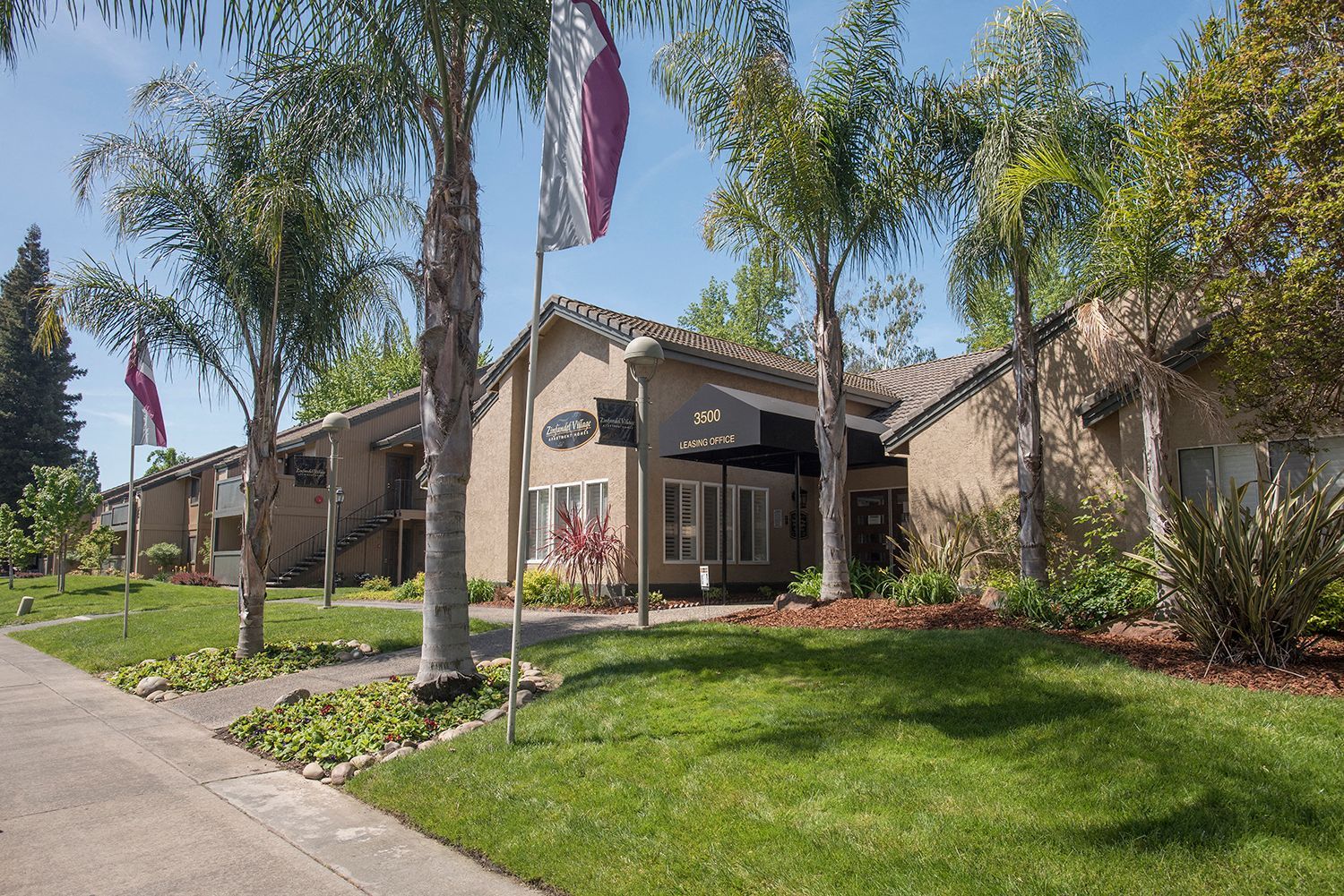 Exterior view of a multifamily complex with a leasing office, palm trees, and landscaping.