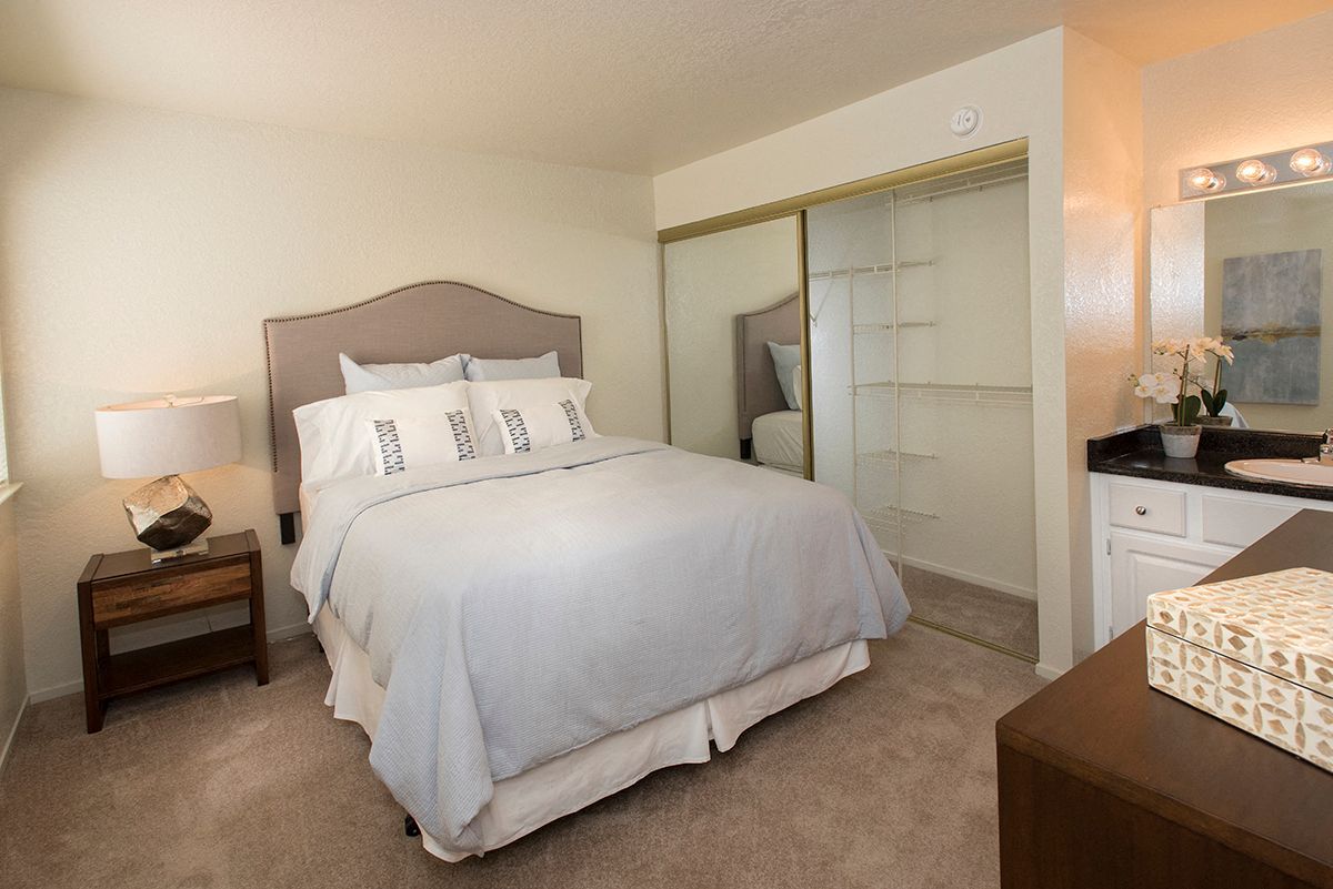 Bedroom in an apartment with a bed, nightstand, mirrored closet doors, and a vanity.