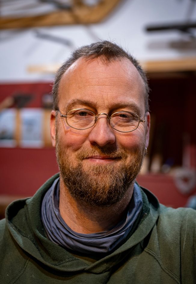 En mand med skæg og briller smiler foran havet.