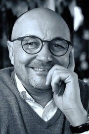 En skaldet mand med briller og skæg smiler på et sort-hvidt foto.