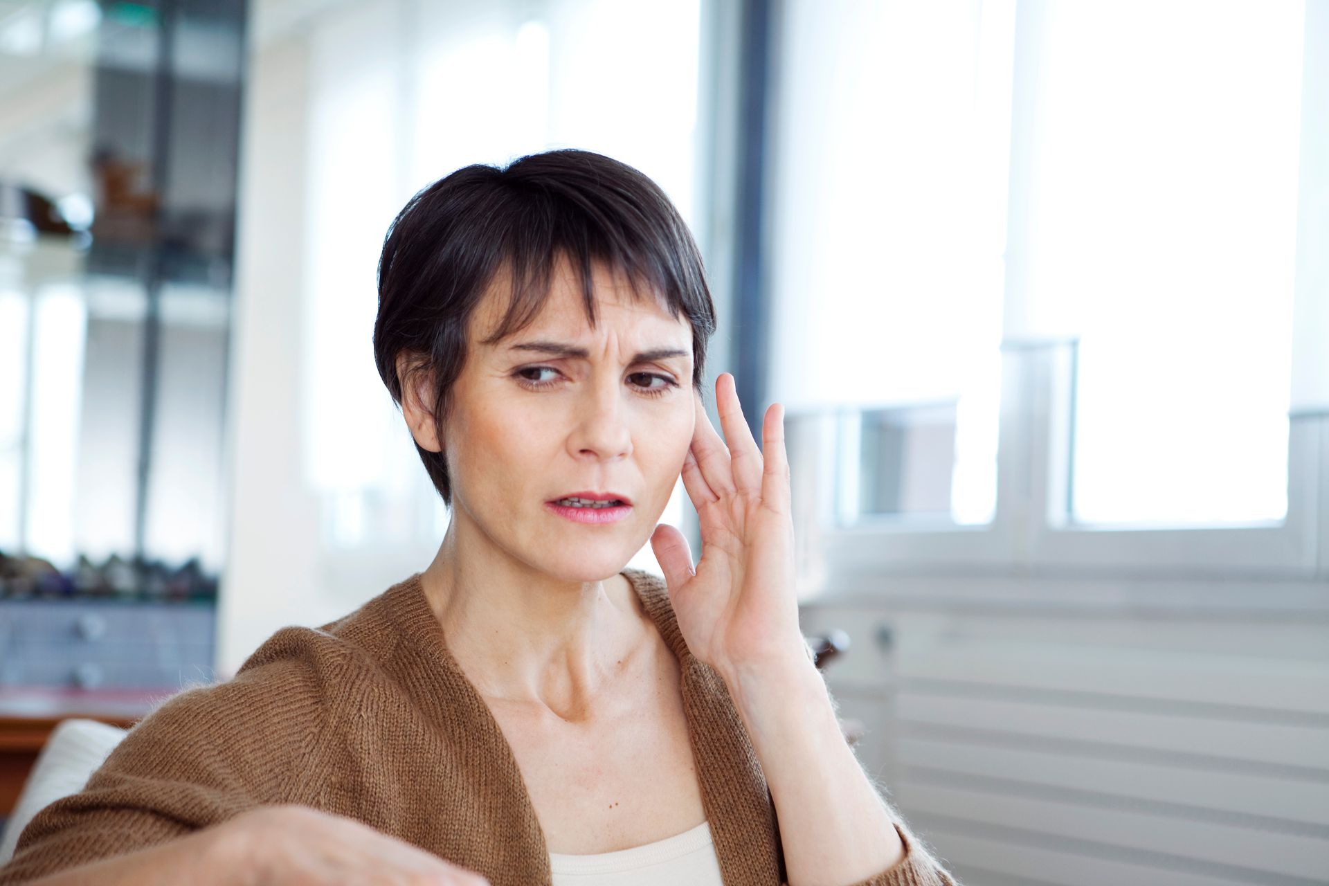 A woman is sitting on a couch with her hand on her ear.