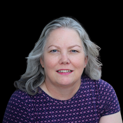 A woman with gray hair is wearing a purple shirt and smiling.