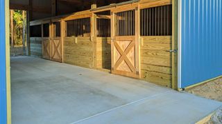 A row of wooden horse stables with a blue building in the background.