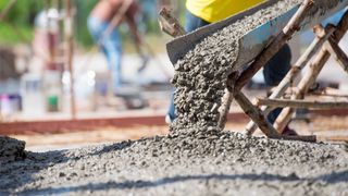 A person is pouring concrete into a wheelbarrow at a construction site.