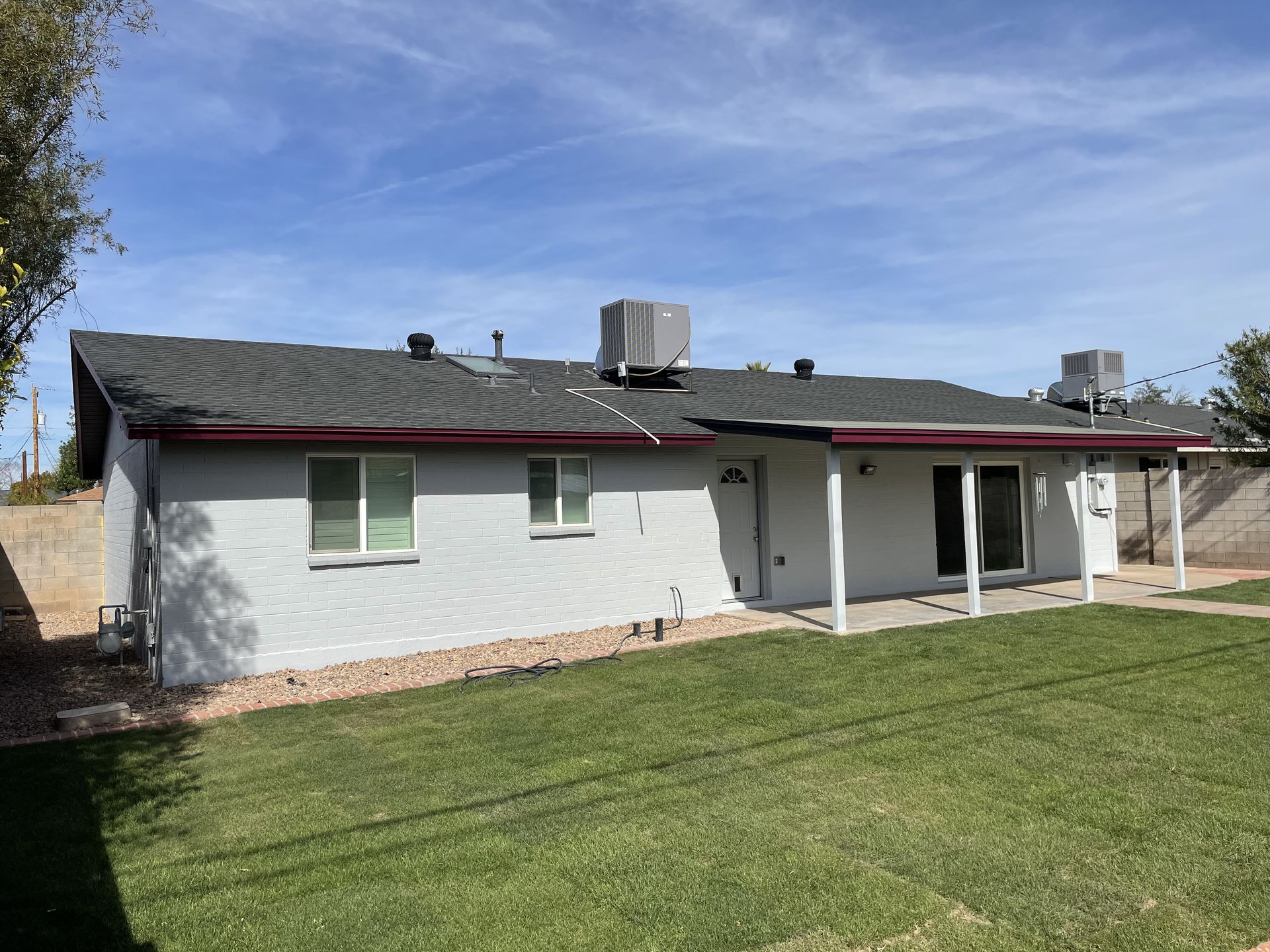 A white house with a gray roof and a large lawn in front of it.