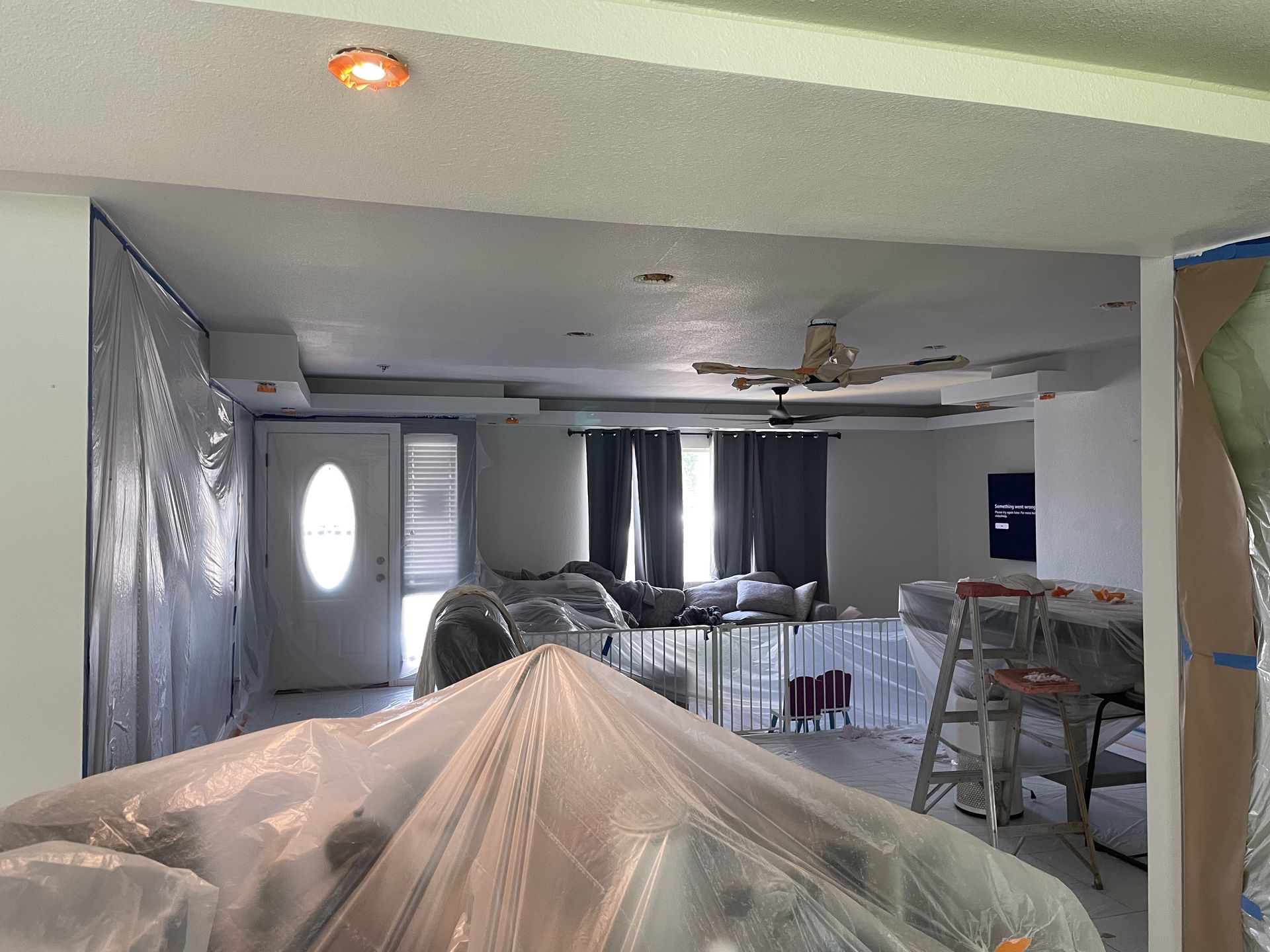 A living room is being painted and covered in plastic.