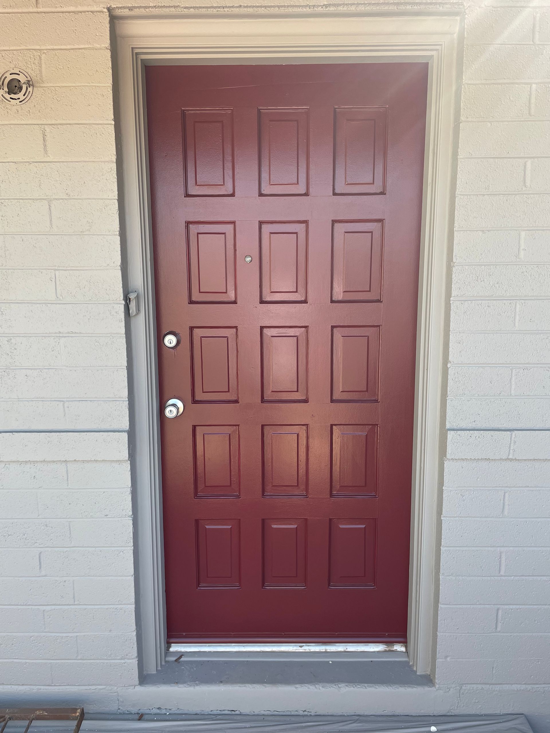 A red door with squares on it is on a brick wall