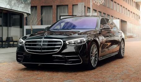 Black luxury Mercedes sedan parked on a brick street beside modern buildings