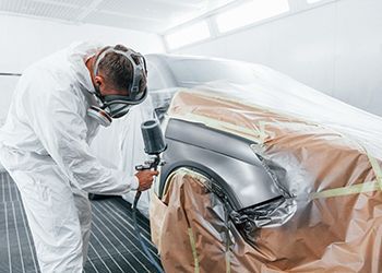 a man is painting a car in a paint booth .