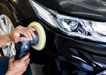 a man is polishing a black car with a polisher .
