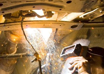 a man is welding a piece of metal under a car .