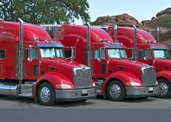 a row of red semi trucks are parked in a parking lot .