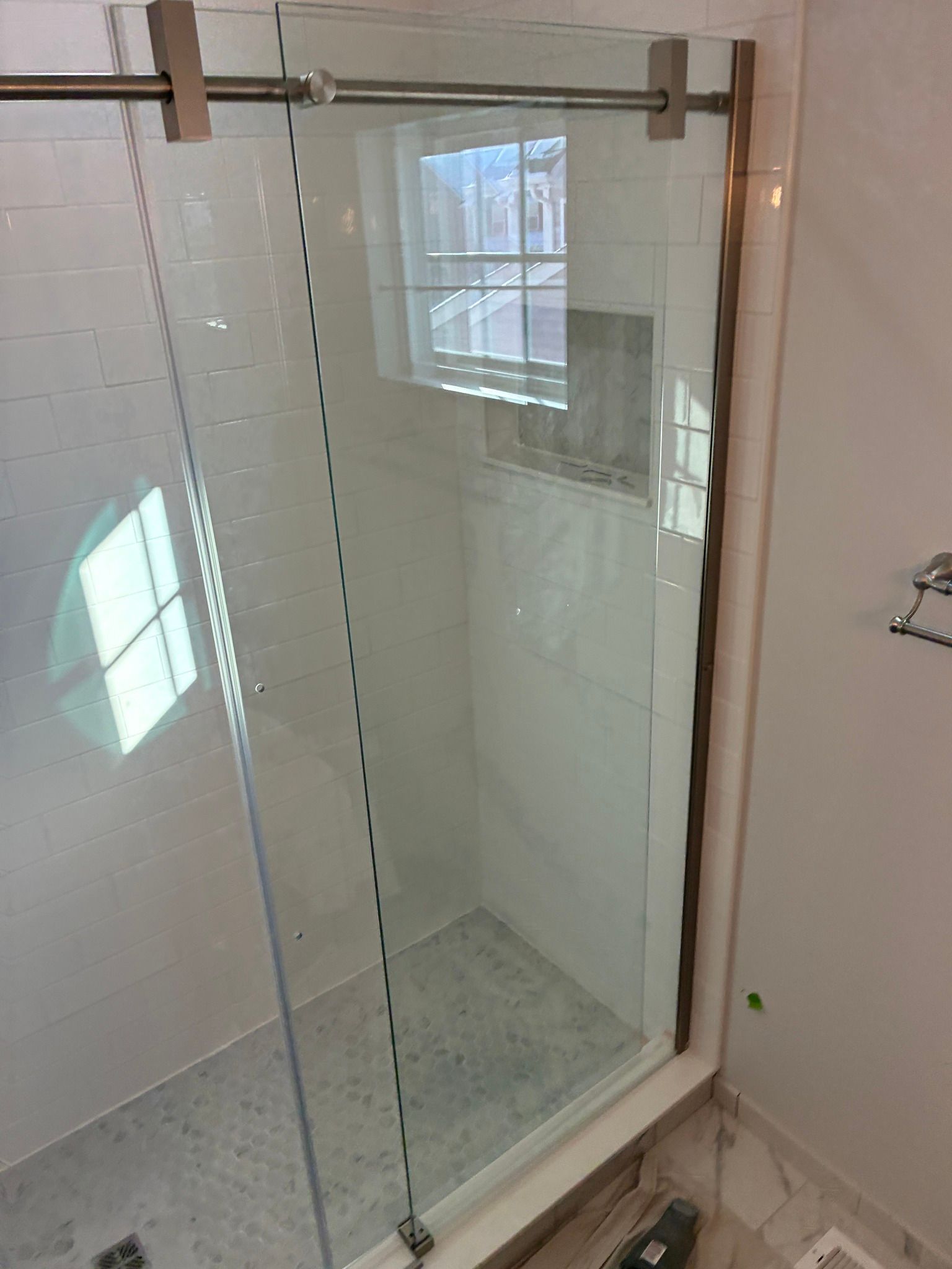 A modern glass shower door with a metal sliding track, installed against white subway tile walls.