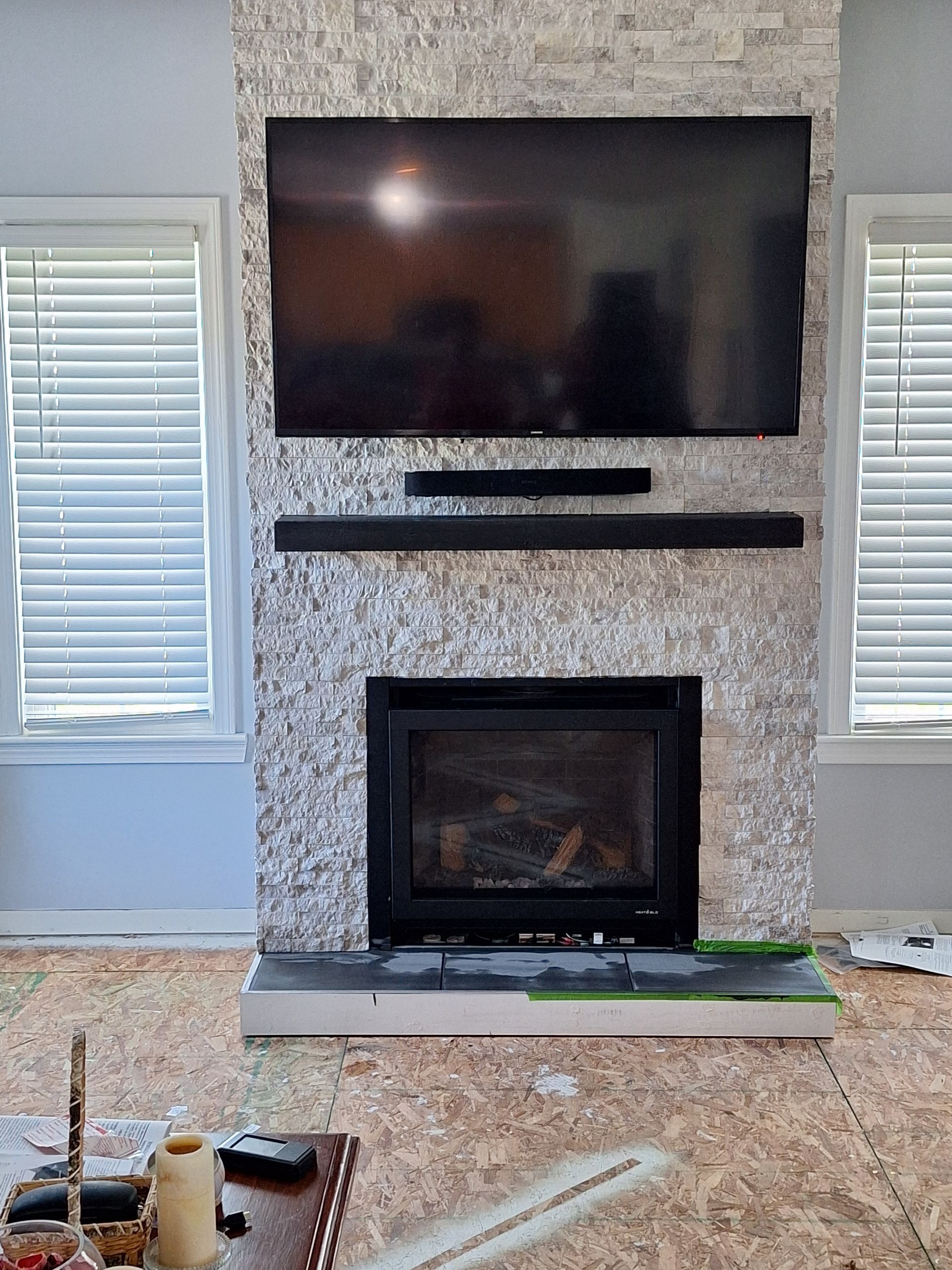 A large television and a black soundbar mounted above a fireplace on a textured, light-colored stone accent wall.