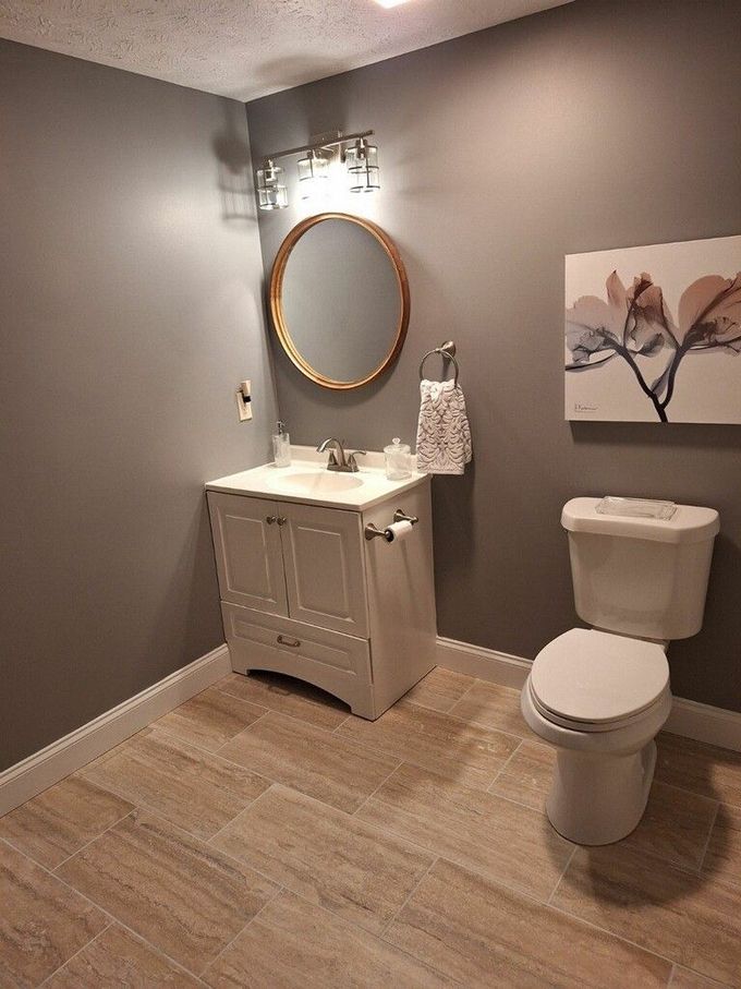 A small bathroom with gray walls, wood-look tile flooring, a white vanity with a round mirror, and a toilet.