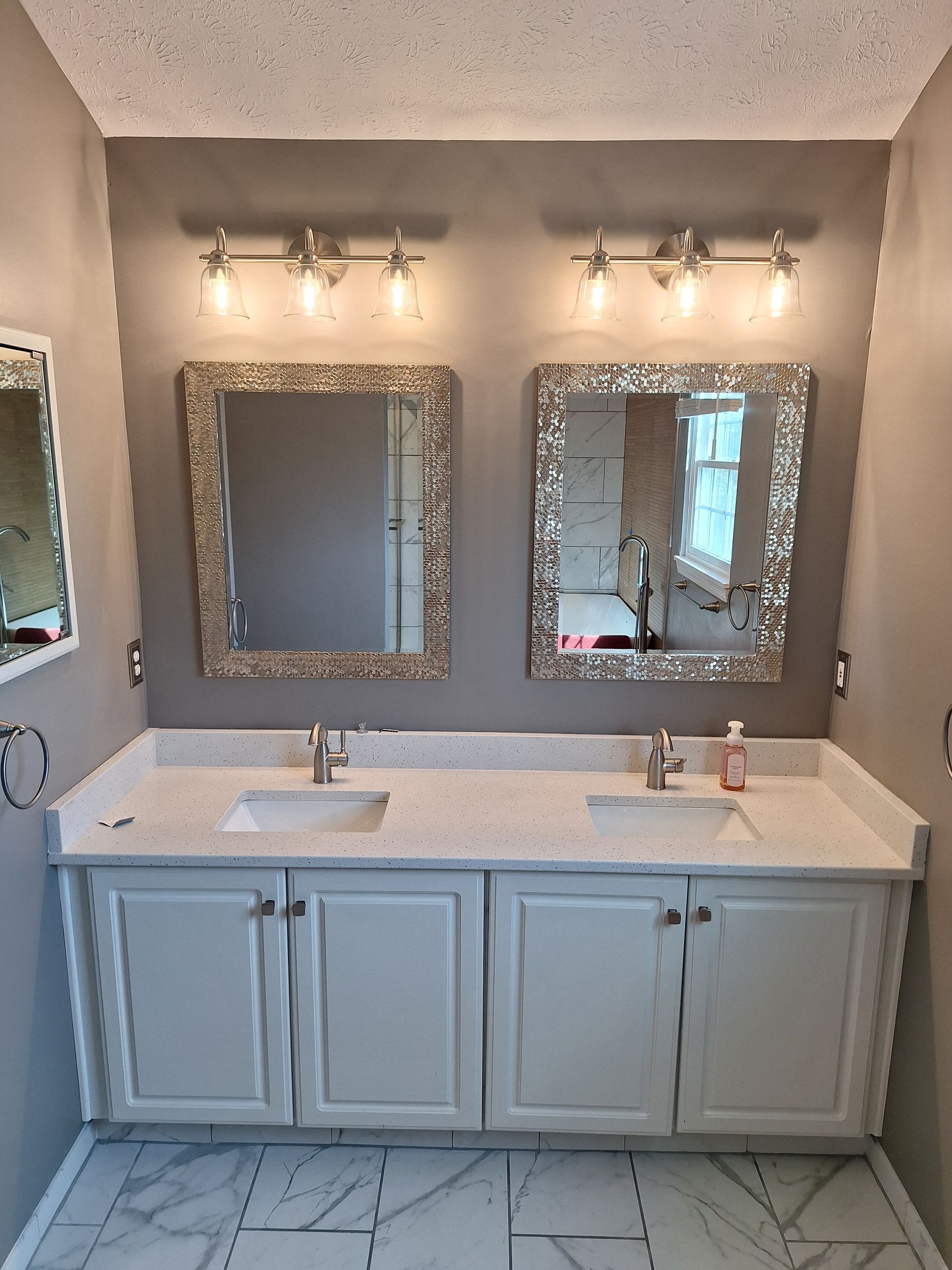 A bathroom with a small, white-trimmed window, taupe walls, a marble-patterned floor, and part of a soaking tub.