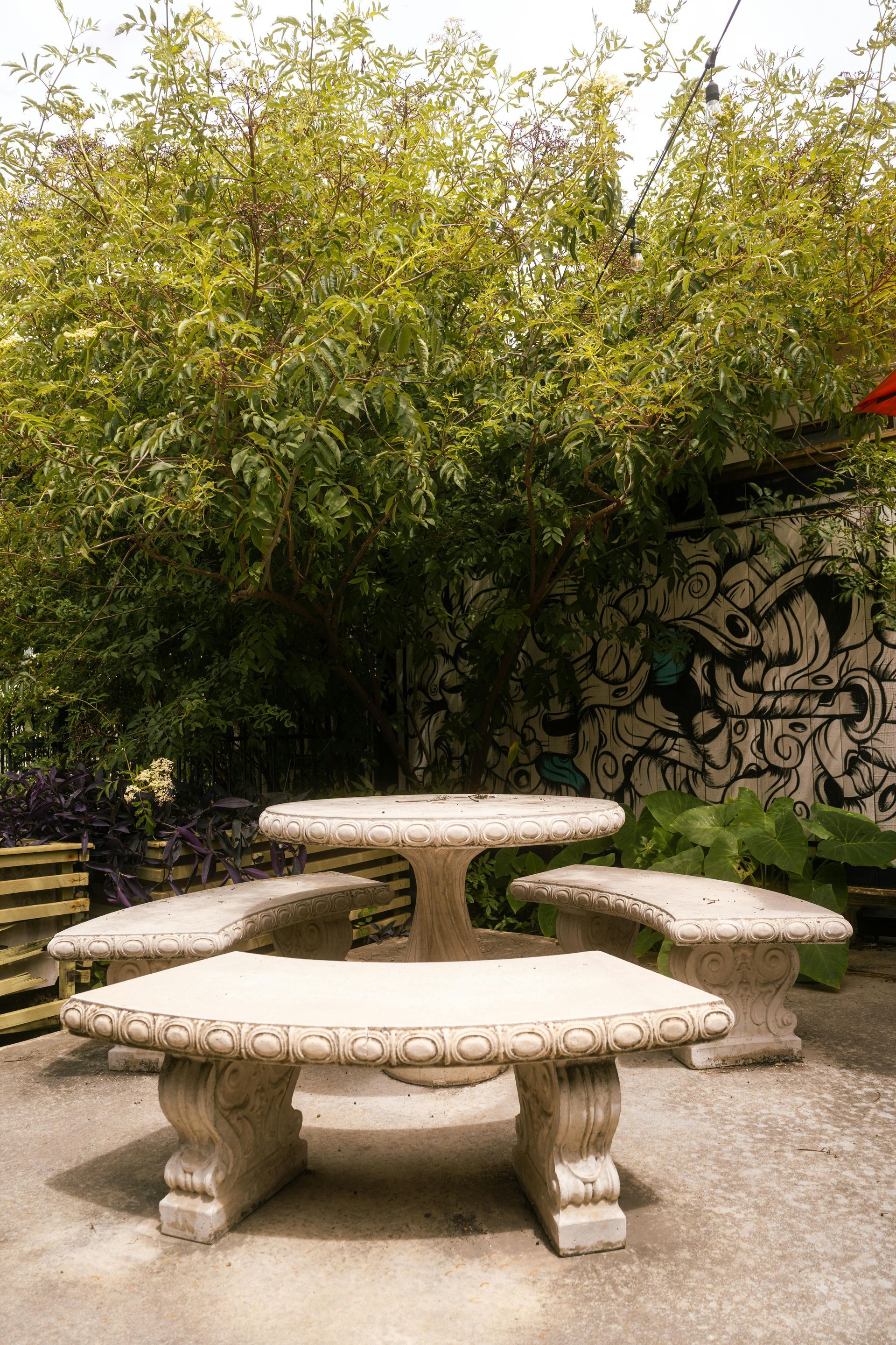 Stone picnic table with attached benches in a shaded outdoor area, next to a wall with a mural.