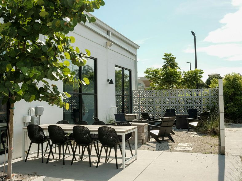 Outdoor patio with a white building, table, black chairs, and fire pit.