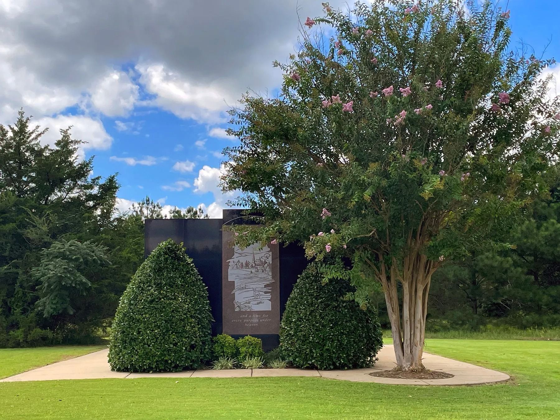 Rendering of a memorial with a central cross and surrounding structures, trees, and sky.