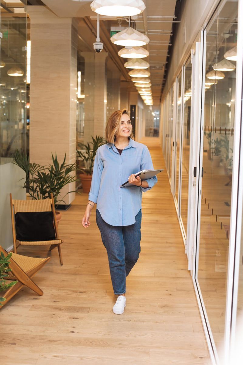 A woman is walking down a hallway holding a tablet.