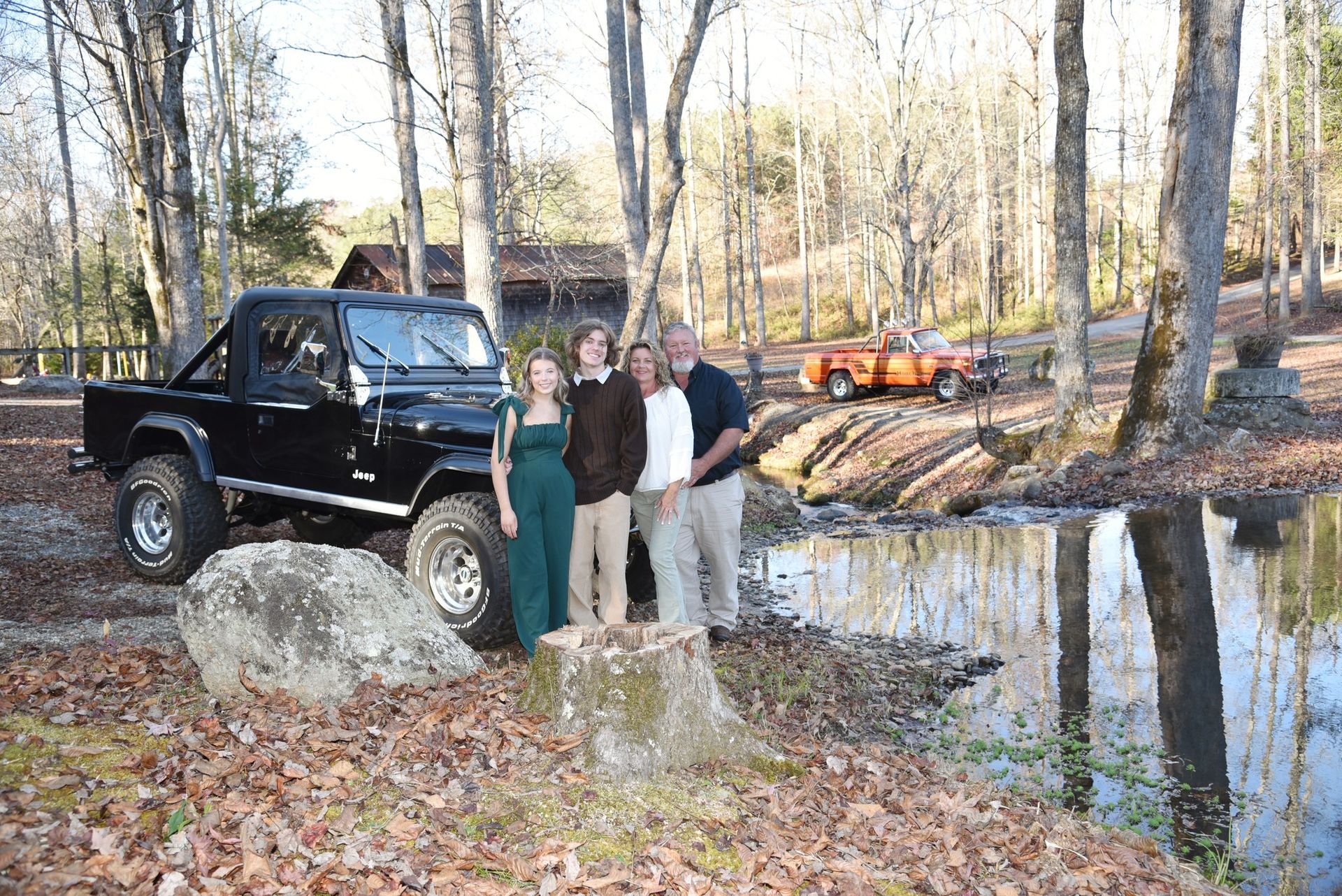A family is posing for a picture in front of a jeep in the woods.
