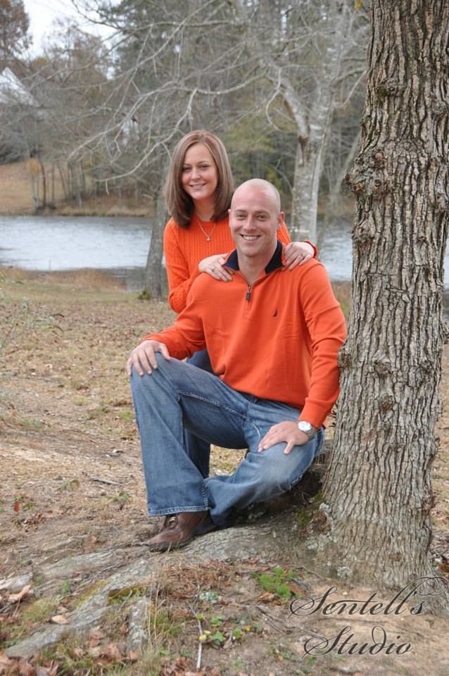 A man and a woman are posing for a picture while sitting next to a tree.