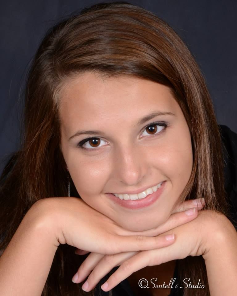A young woman with her head resting on her hands smiles for the camera
