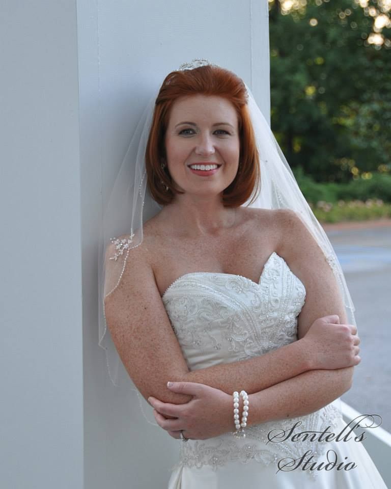 A woman in a wedding dress is leaning against a wall and smiling.