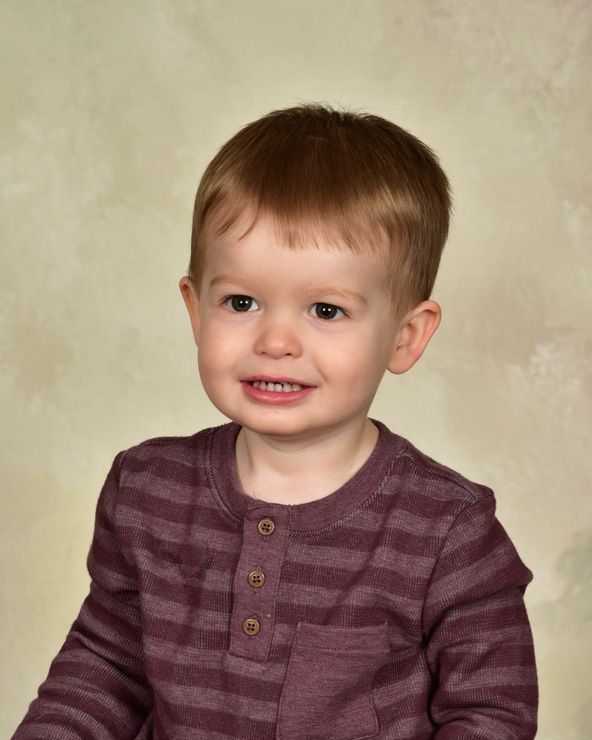 A young boy wearing a purple striped shirt is smiling for the camera.