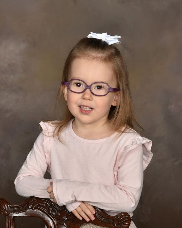 A little girl wearing glasses is sitting on a chair