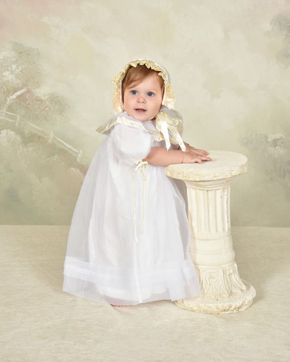 A baby in a white dress is sitting on a pedestal