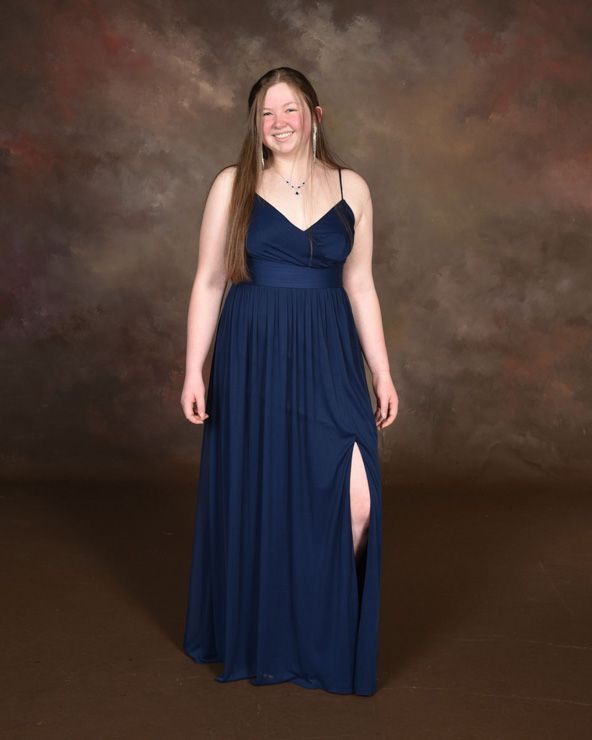 A woman in a long blue dress is standing in front of a brown background.