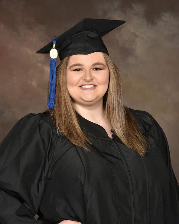 A woman wearing a graduation cap and gown is smiling for the camera.