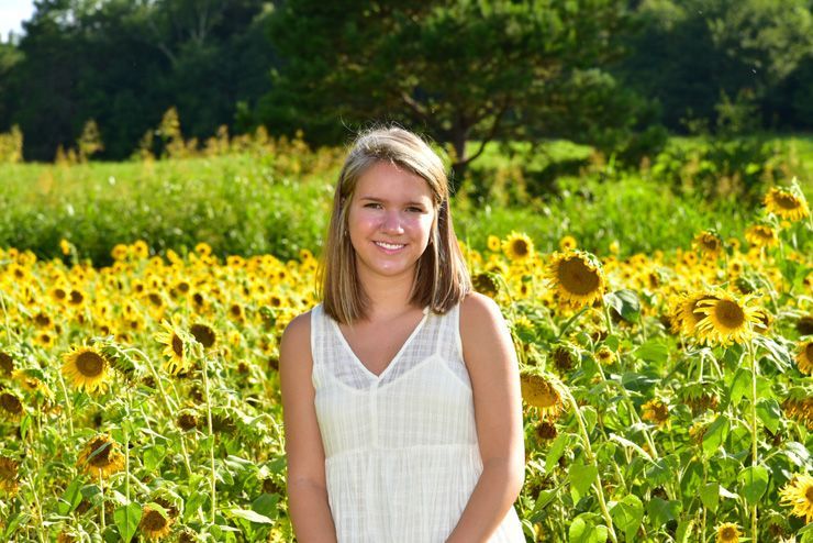 A young girl in a white dress is standing in a field of sunflowers.