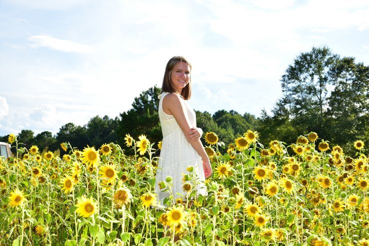 A woman in a white dress is standing in a field of sunflowers.