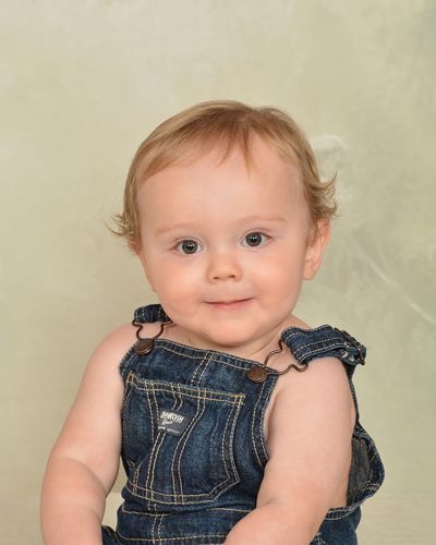A baby is wearing overalls and smiling for the camera