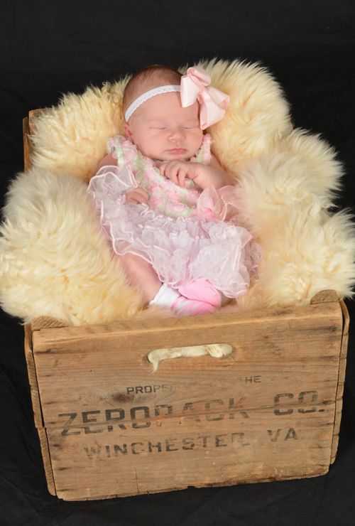 A baby in a pink dress is sleeping in a wooden box.