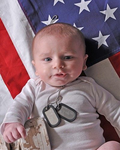A baby wearing a dog tag laying in front of an american flag