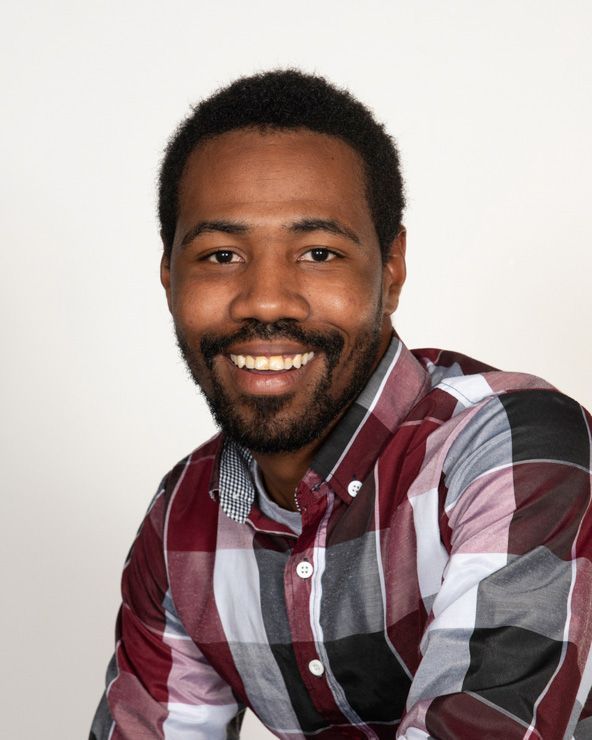 A man with a beard wearing a plaid shirt is smiling for the camera.