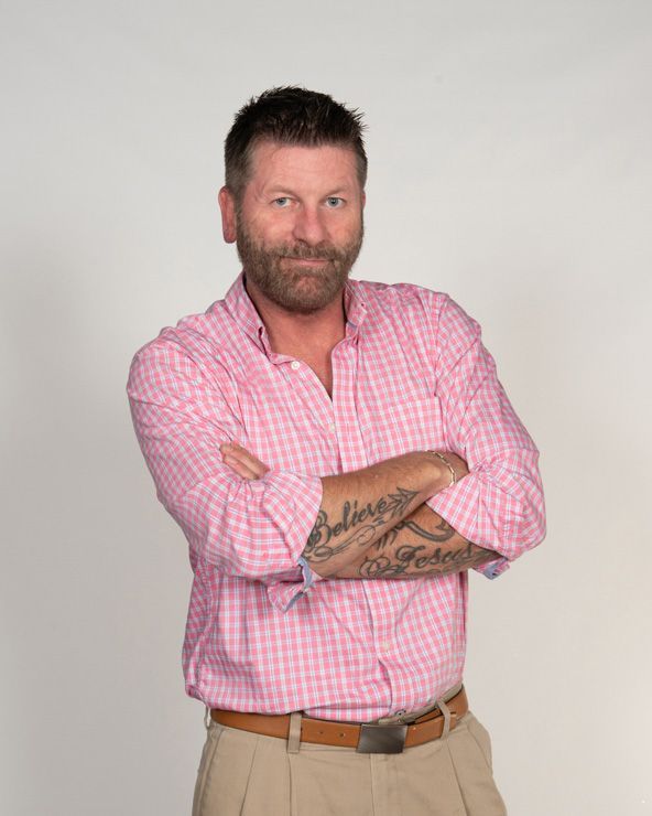 A man with a beard and tattoos is standing with his arms crossed.