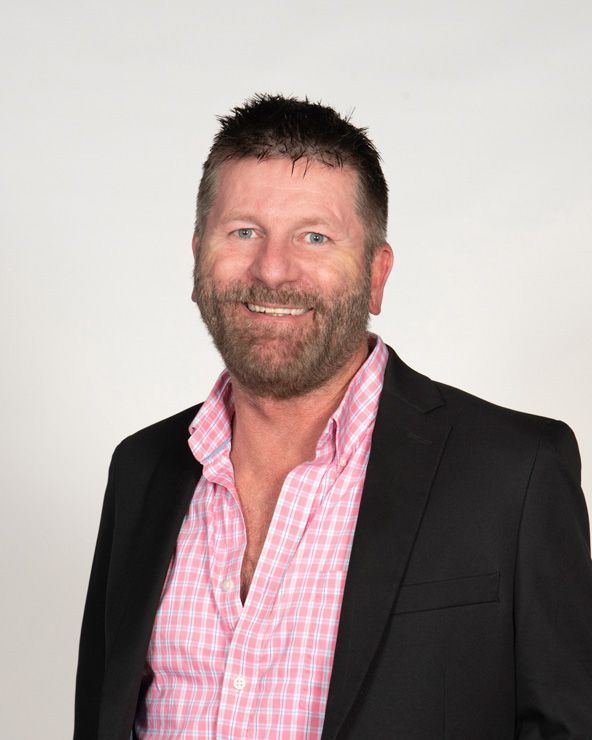 A man in a suit and pink plaid shirt is smiling for the camera.