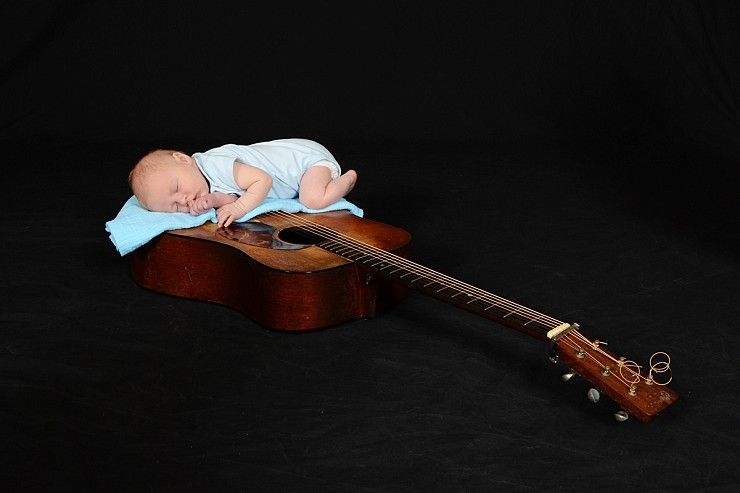 A baby is sleeping on top of an acoustic guitar.