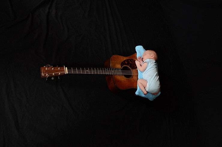 A baby is sleeping on top of an acoustic guitar.