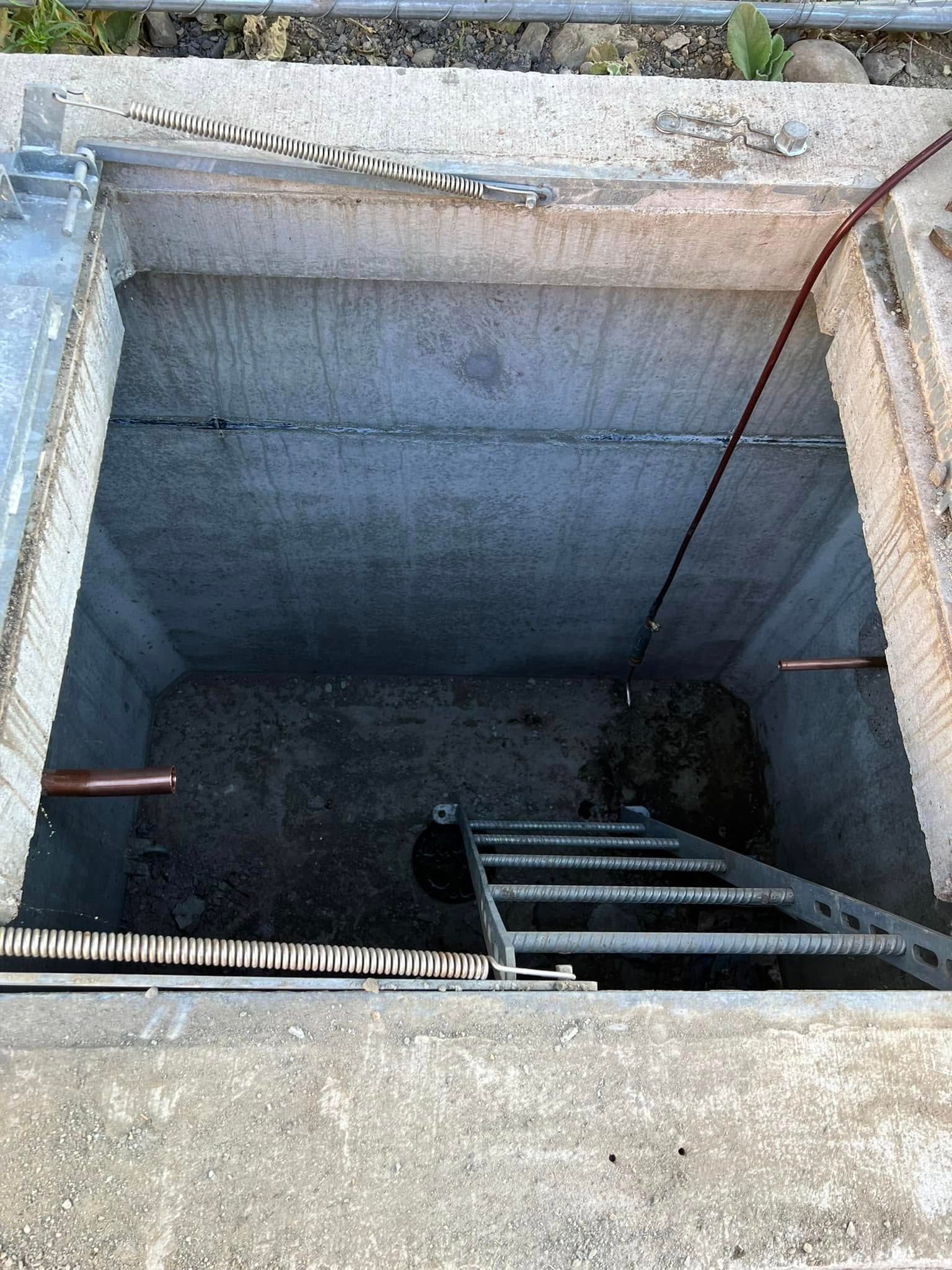 A deep, rectangular concrete utility vault with a metal ladder leading down into a dark, shadowed space.