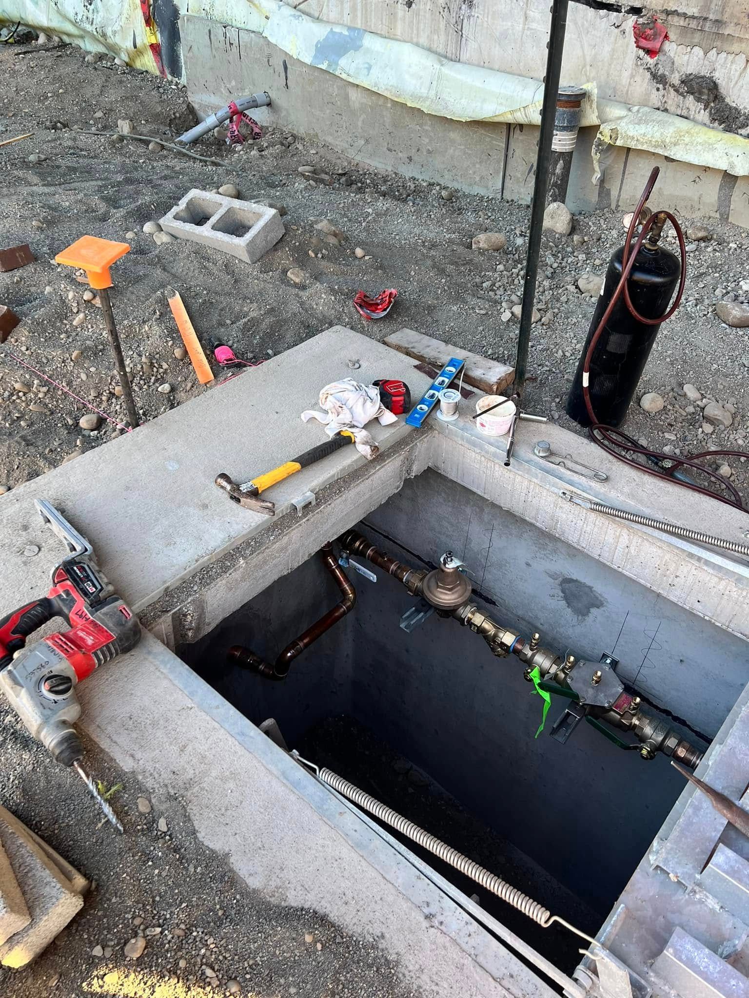 Construction site with a concrete meter vault, plumbing tools, and pipes exposed in the ground.