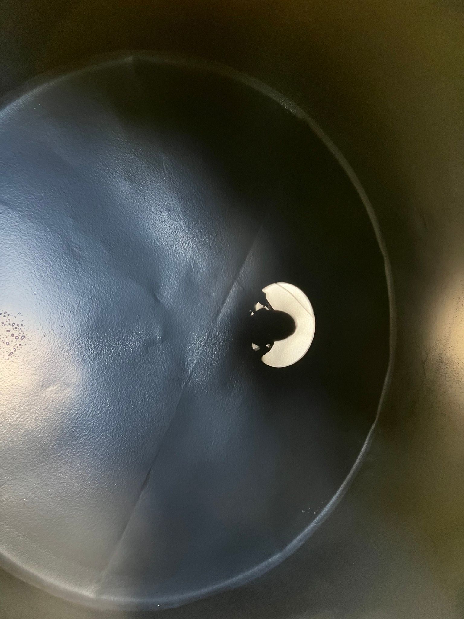 Looking down into a dark, round container or barrel with a single white circular object at the bottom.