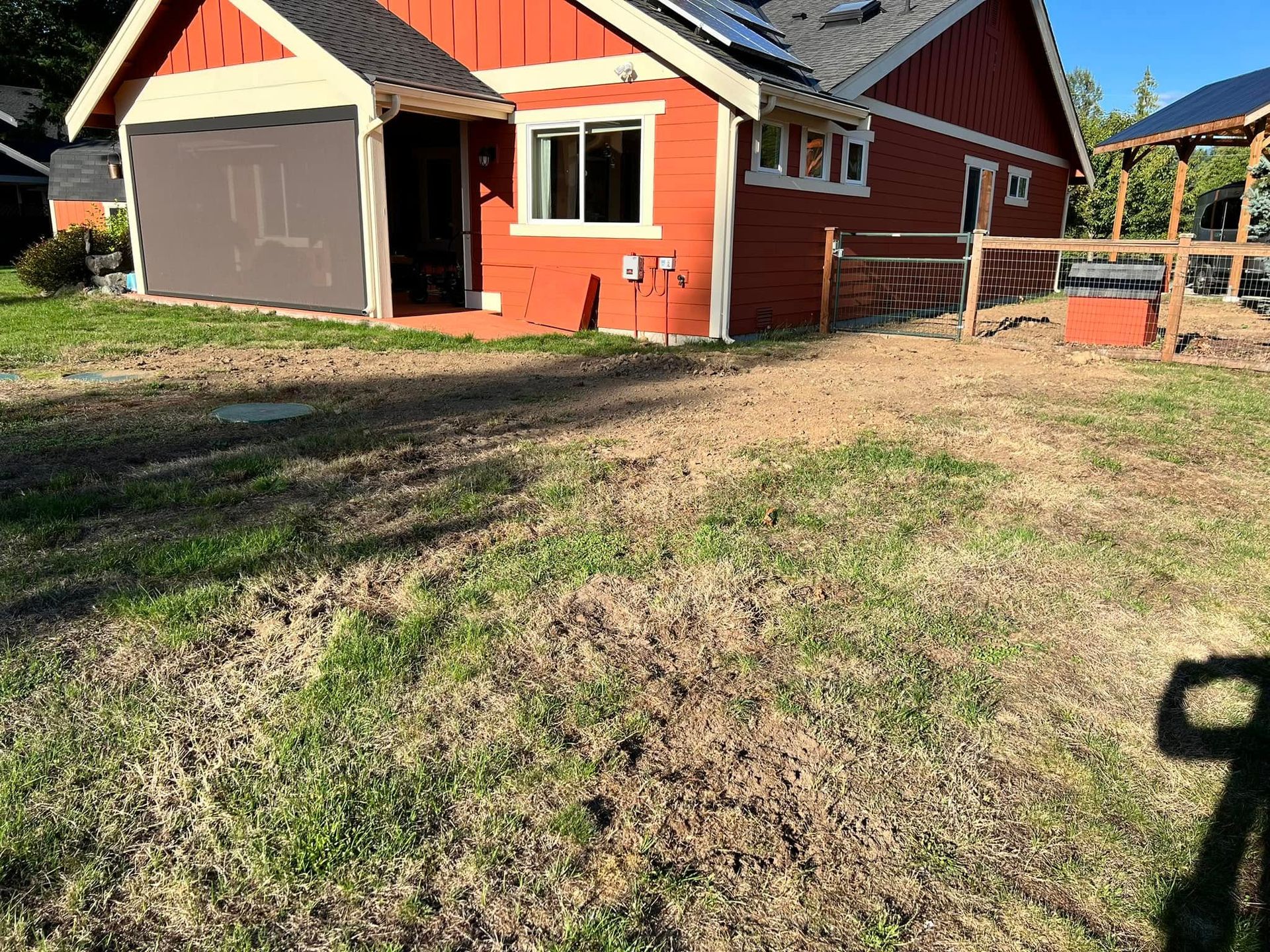 A red house with a large gray sun shade over the patio, surrounded by a lawn under a clear blue sky.