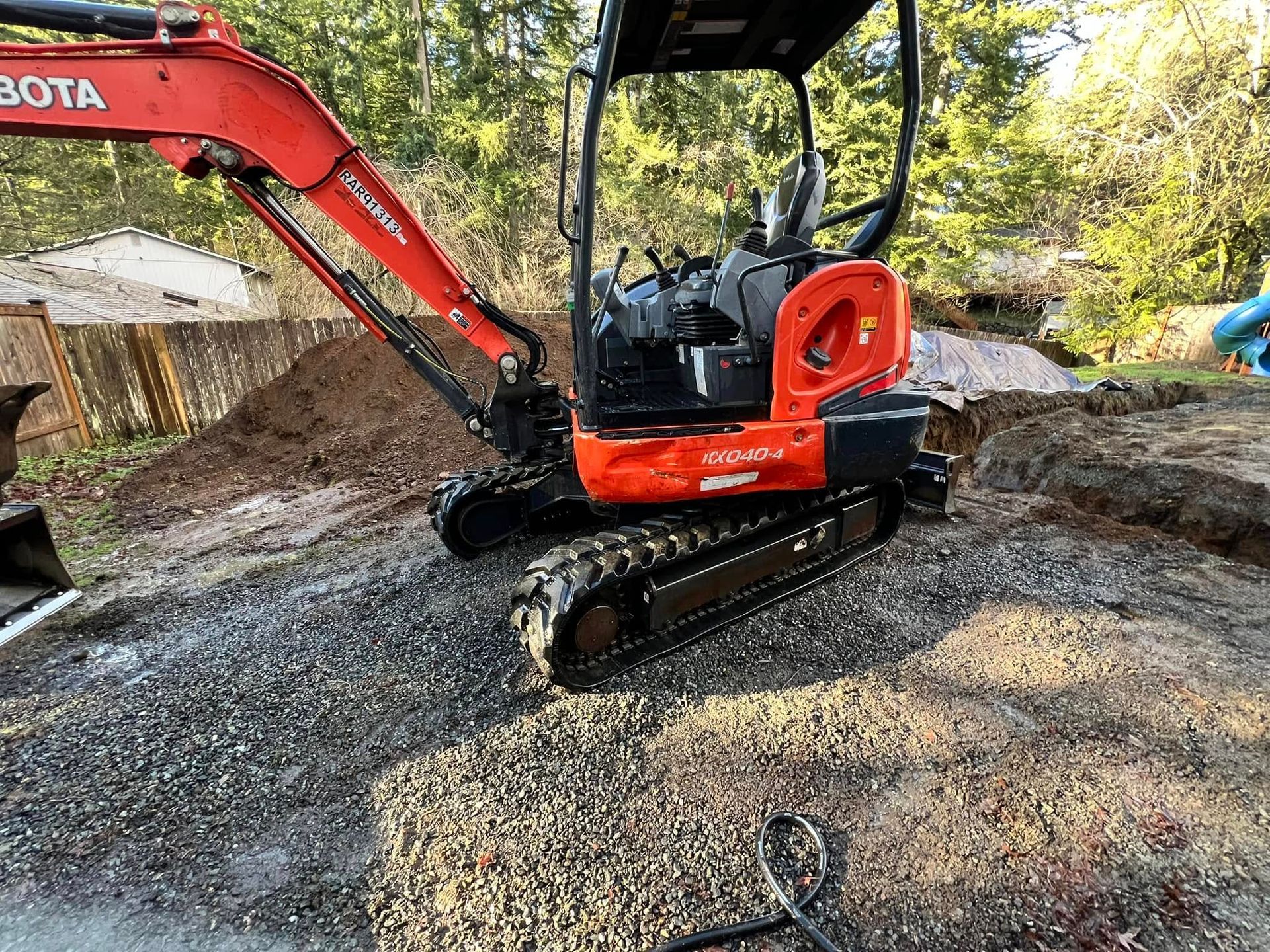 An orange Kubota compact excavator parked on a gravel surface outdoors with a dirt pile in the background.